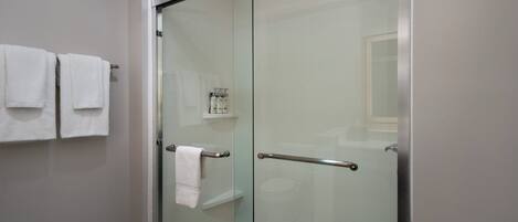 Un baño moderno con cabina de ducha de vidrio, un perchero con dos toallas blancas y una pequeña estantería con artículos de aseo.
