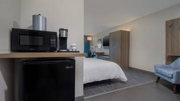 A hotel room with a bed, a desk with a microwave, a refrigerator, a chair, and a wardrobe.