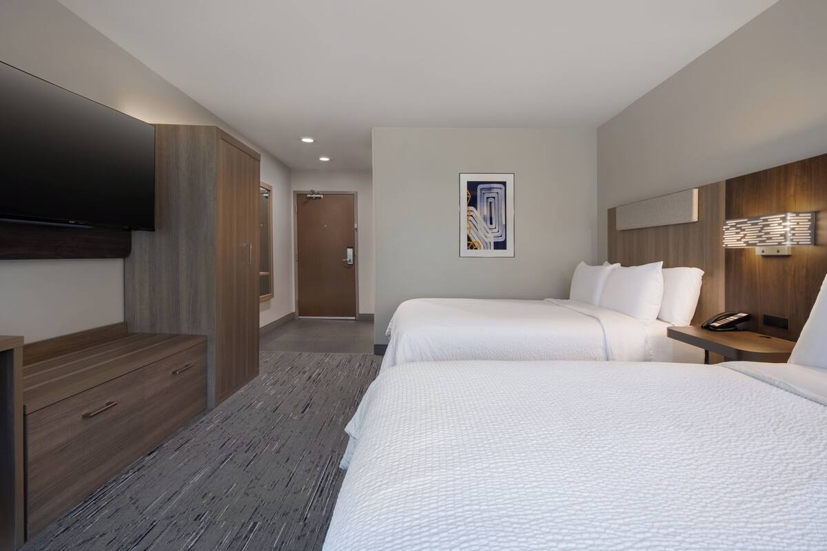 A hotel room with two beds, a flat-screen TV, a wooden wardrobe, a painting on the wall, and a bedside table with a phone.