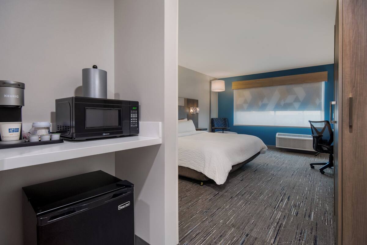 A hotel room with a bed, a desk, a microwave, a coffee maker, and a projector screen.