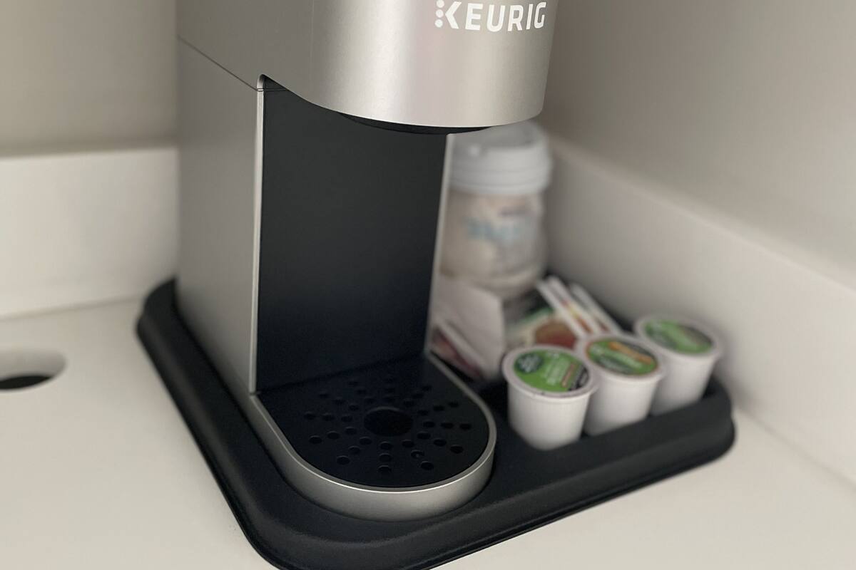A Keurig coffee machine with a drip tray and coffee pods on a white countertop.