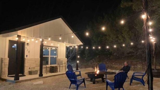 Une terrasse extérieure agrémentée de guirlandes lumineuses, d’un foyer et de chaises bleues.