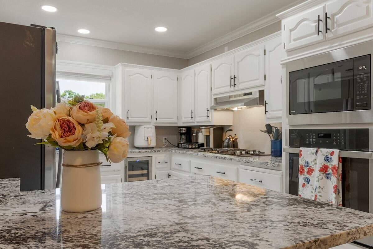 A modern kitchen with white cabinets, granite countertops, and stainless steel appliances.