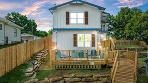 Une maison à deux étages dotée d’une terrasse en bois, d’un mur de soutènement en pierre et d’un escalier menant à un deuxième niveau.
