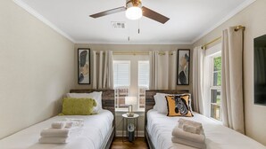 Une chambre d’hôtel avec deux lits, un ventilateur de plafond, une petite table avec une lampe et une vue sur l’extérieur par les fenêtres.