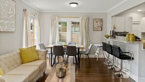 Un salon moderne comprenant un canapé, une table à manger, des chaises et un coin cuisine avec des tabourets de bar.