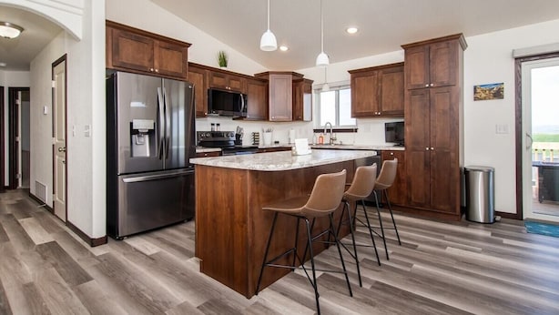 A modern kitchen with a large island, stainless steel appliances, wooden cabinets, and a bar stool seating area.