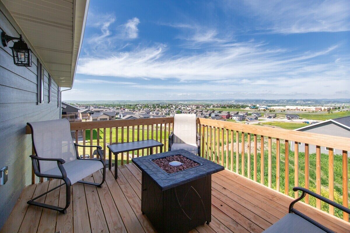 A wooden deck with a fire pit, outdoor seating, and a view of a residential area.