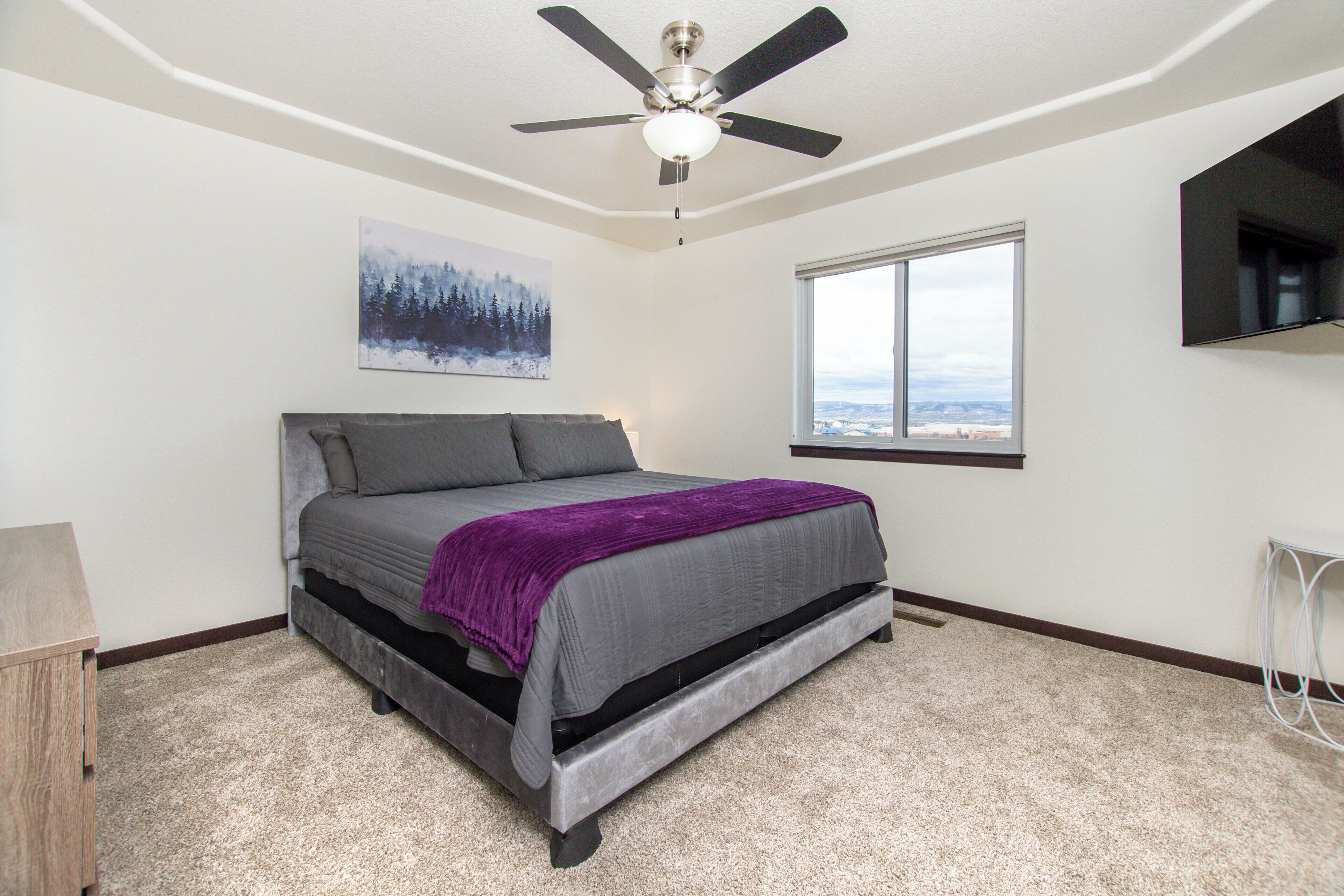 Un dormitorio con cama, ventilador de techo, ventana con vistas y televisor instalado.