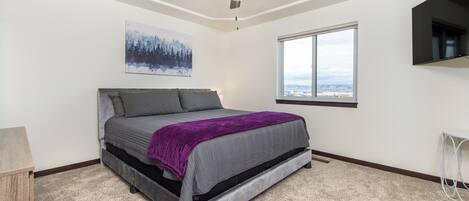 Un dormitorio con cama, ventilador de techo, ventana con vistas y televisor instalado.