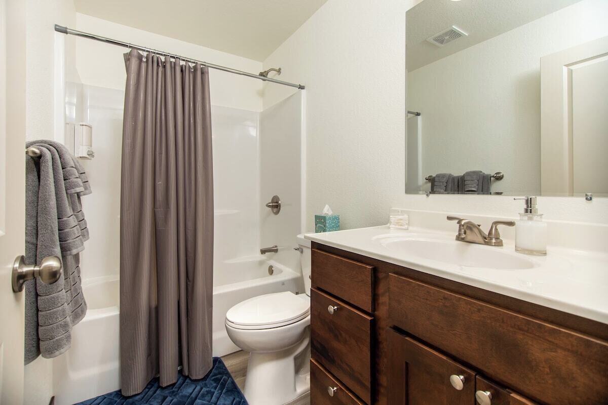 A bathroom with a bathtub, toilet, vanity with drawers, and a large mirror.