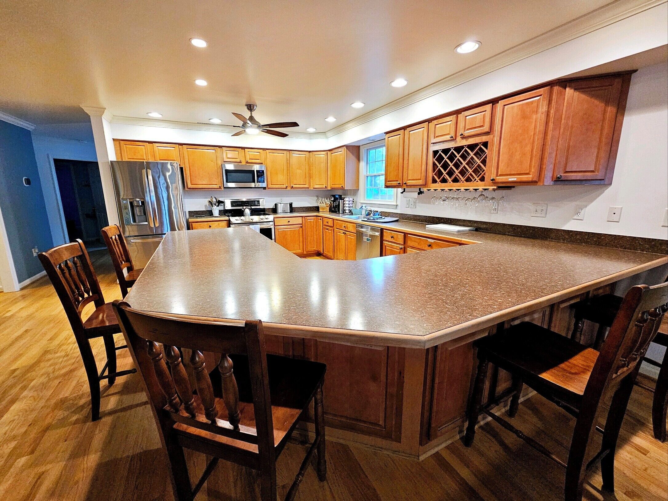 A modern kitchen with a large island, wooden cabinets, stainless steel appliances, and a ceiling fan.