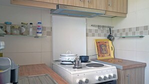 Una cocina con estufa blanca, una olla sobre la hornilla y un estante con frascos y botellas.