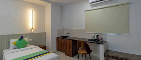 A hotel room with a bed, a desk, a chair, a sink, and an air conditioning unit.