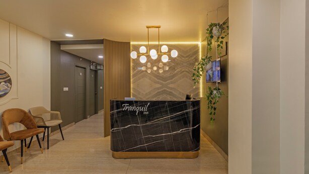 A reception desk with a marble top and a sign that reads "Tranquil inn". There are two chairs with gold legs, a wall-mounted TV, and a hanging plant. - Treebo Raghavendra Tranquil Inn Bellandur (Bengaluru)