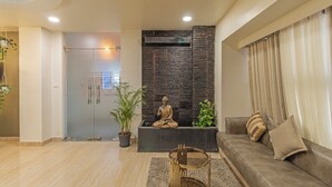 A modern living room with a Buddha statue, a sofa, a coffee table, and a potted plant. - Treebo Raghavendra Tranquil Inn Bellandur (Bengaluru)