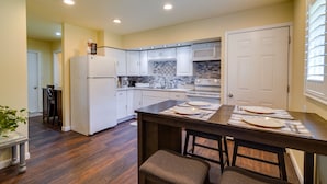 A modern kitchen with white cabinets, a central island with stools, and a dining table set for four. - Sunny California Retreat w/ Pool Access & Patio! (Shasta Lake)