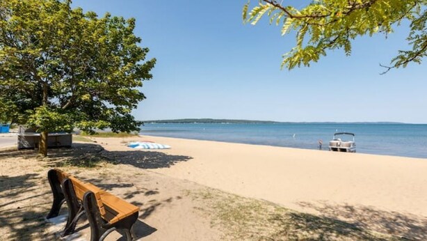 A beach with a bench, a boat, and a clear view of the water. - Eclectic Cottage by the bay, downtown, bike trail (Traverse City)