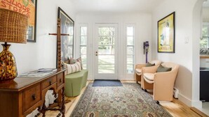 A well-lit hallway with a wooden floor, a green bench, a patterned rug, and a door leading outside. - Eclectic Cottage by the bay, downtown, bike trail (Traverse City)