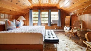 A cozy attic bedroom with a wooden ceiling, a large bed, a small table, and two wicker chairs. - Eclectic Cottage by the bay, downtown, bike trail (Traverse City)