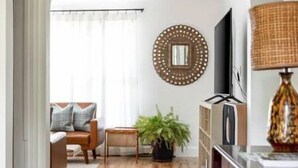 A living room with a wooden floor, a sofa, a coffee table, a TV, and a decorative mirror. - Eclectic Cottage by the bay, downtown, bike trail (Traverse City)