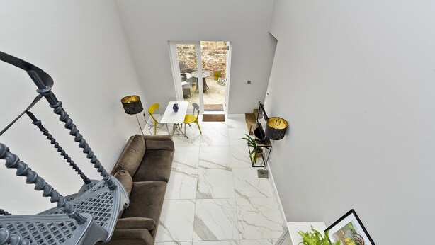 A modern interior with a staircase, a sofa, a dining area with chairs, and a view of the outside.