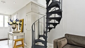 A spiral staircase with black railings, a wooden bench, a white console table with a vase of flowers, and a brown sofa.