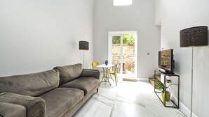 A modern living room with a grey sofa, a TV on a stand, and a dining area with a yellow chair.