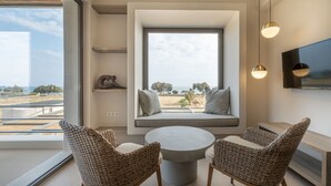 Un salon moderne doté d’une grande fenêtre, de meubles en osier, d’une table ronde et d’un téléviseur à écran plat fixé au mur.