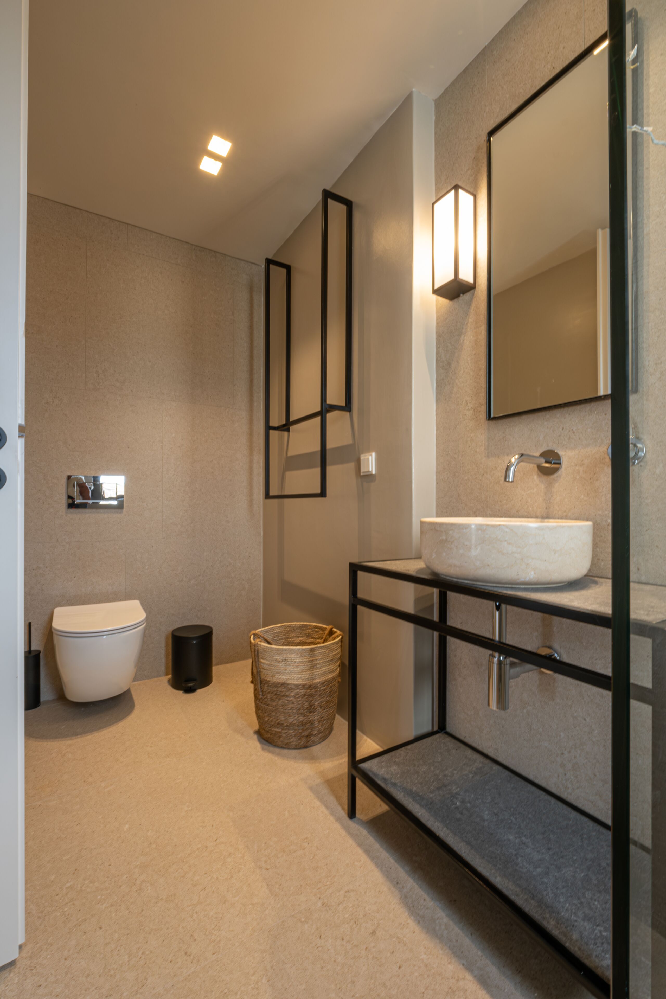 Une salle de bain moderne avec des toilettes blanches, un grand miroir et un lavabo doté d’un cadre noir.