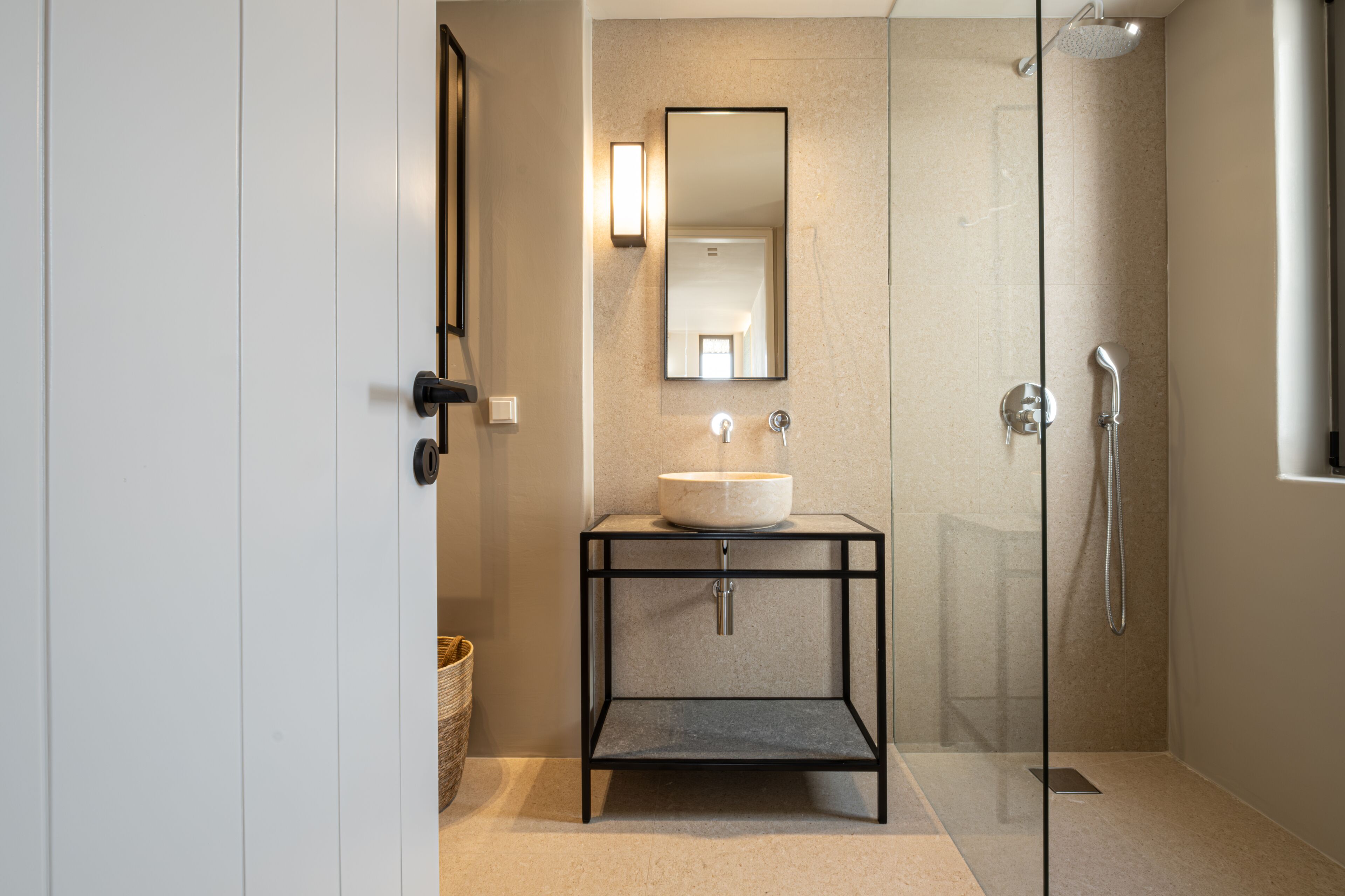 A modern bathroom with a glass-enclosed shower, a pedestal sink with a mirror, and a small shelf.