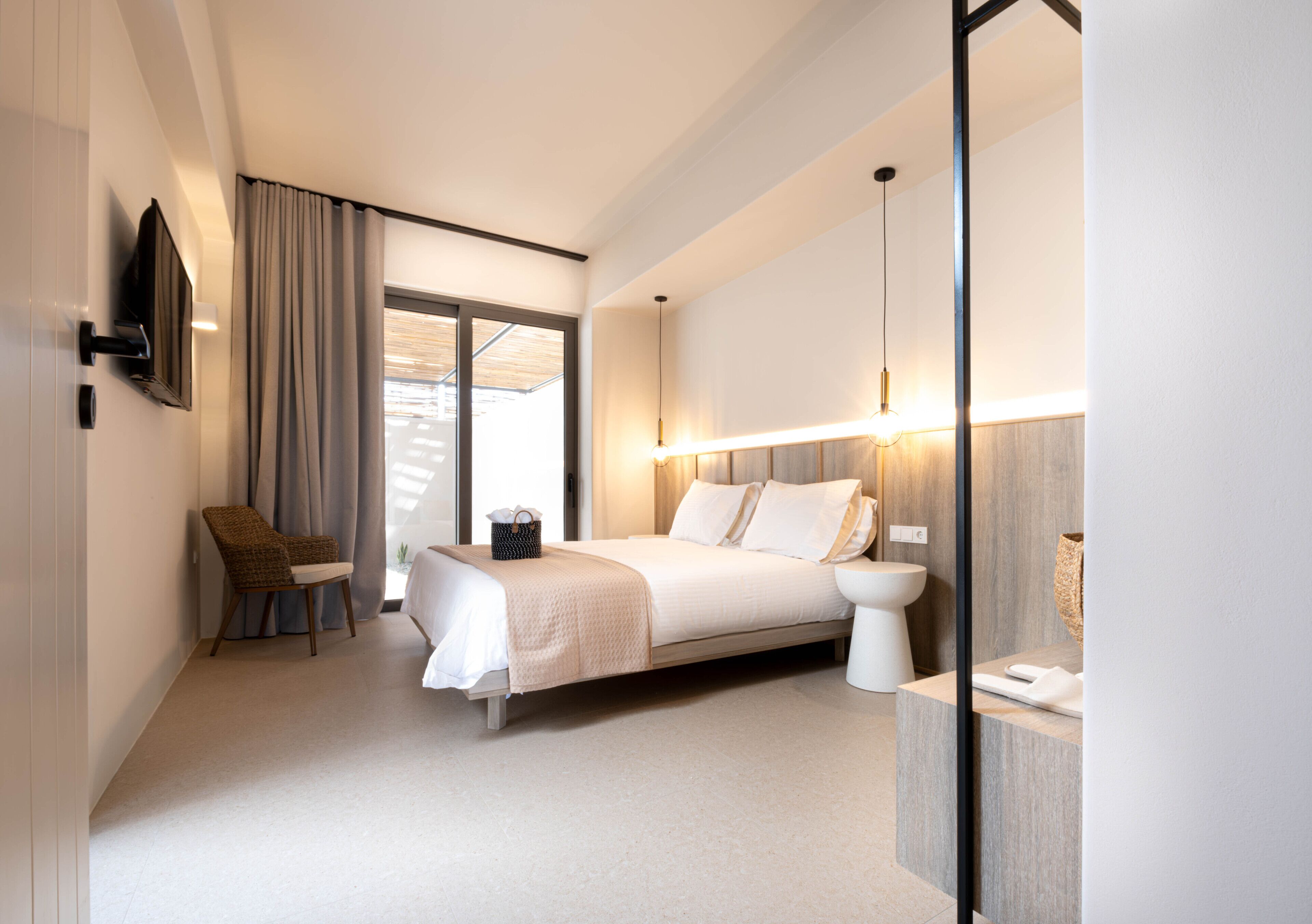 A modern hotel room with a bed, a chair, a bedside table, and a television mounted on the wall.