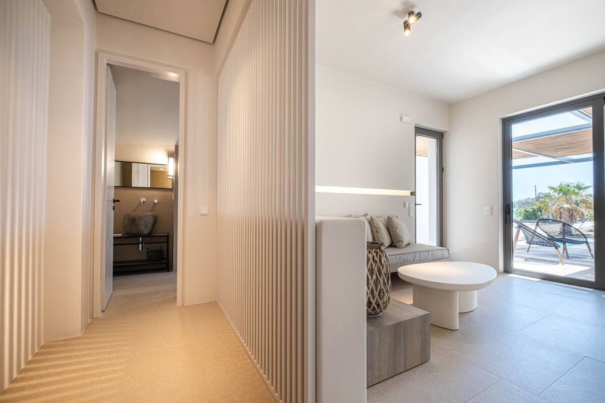 Een modern interieur met een gang die leidt naar een eetgedeelte, een zithoek met een ronde tafel, en uitzicht op de omgeving.