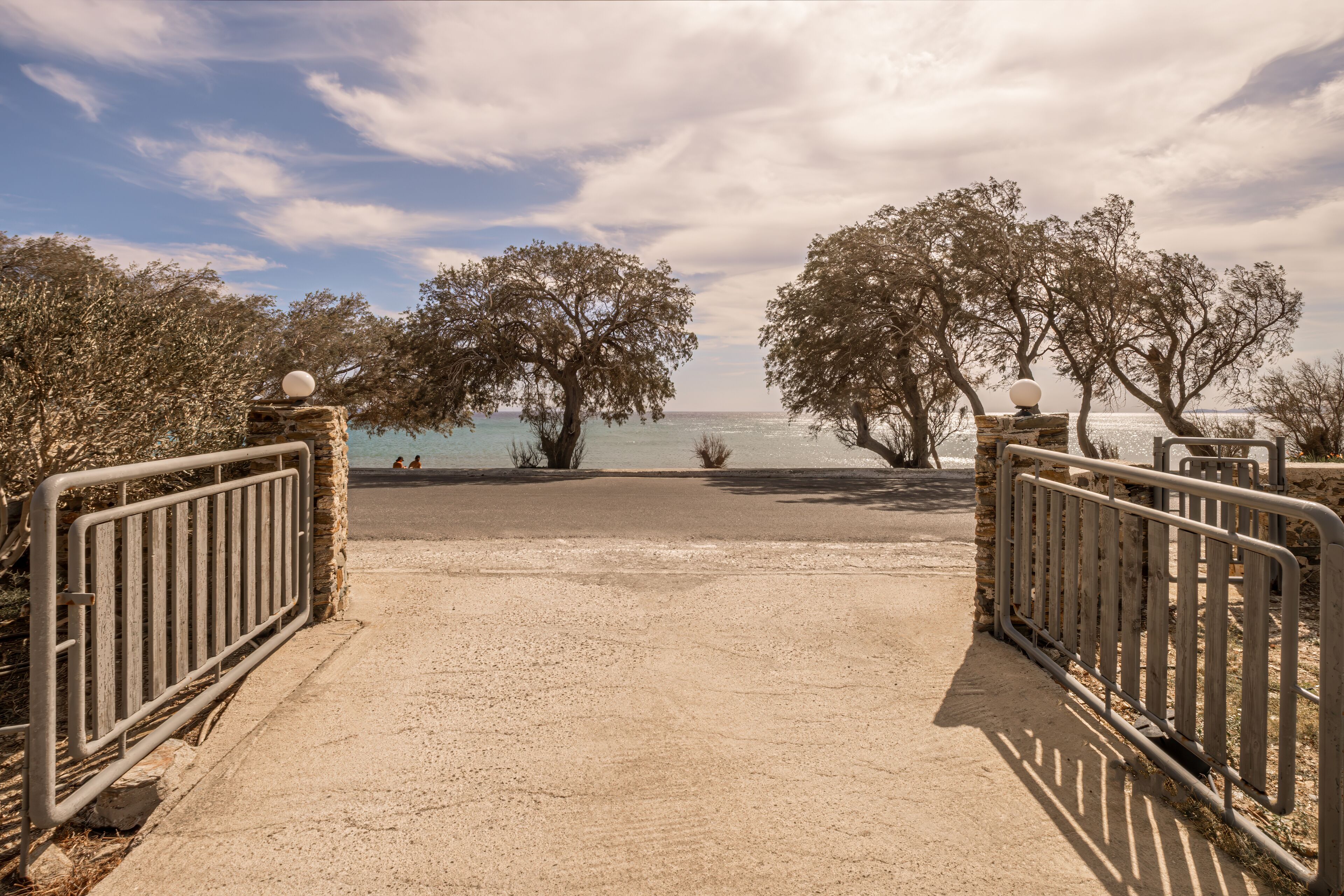 A beach entrance with a metal gate, trees, and a view of the sea.