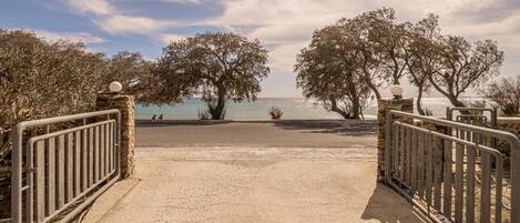 A beach entrance with a metal gate, trees, and a view of the sea.