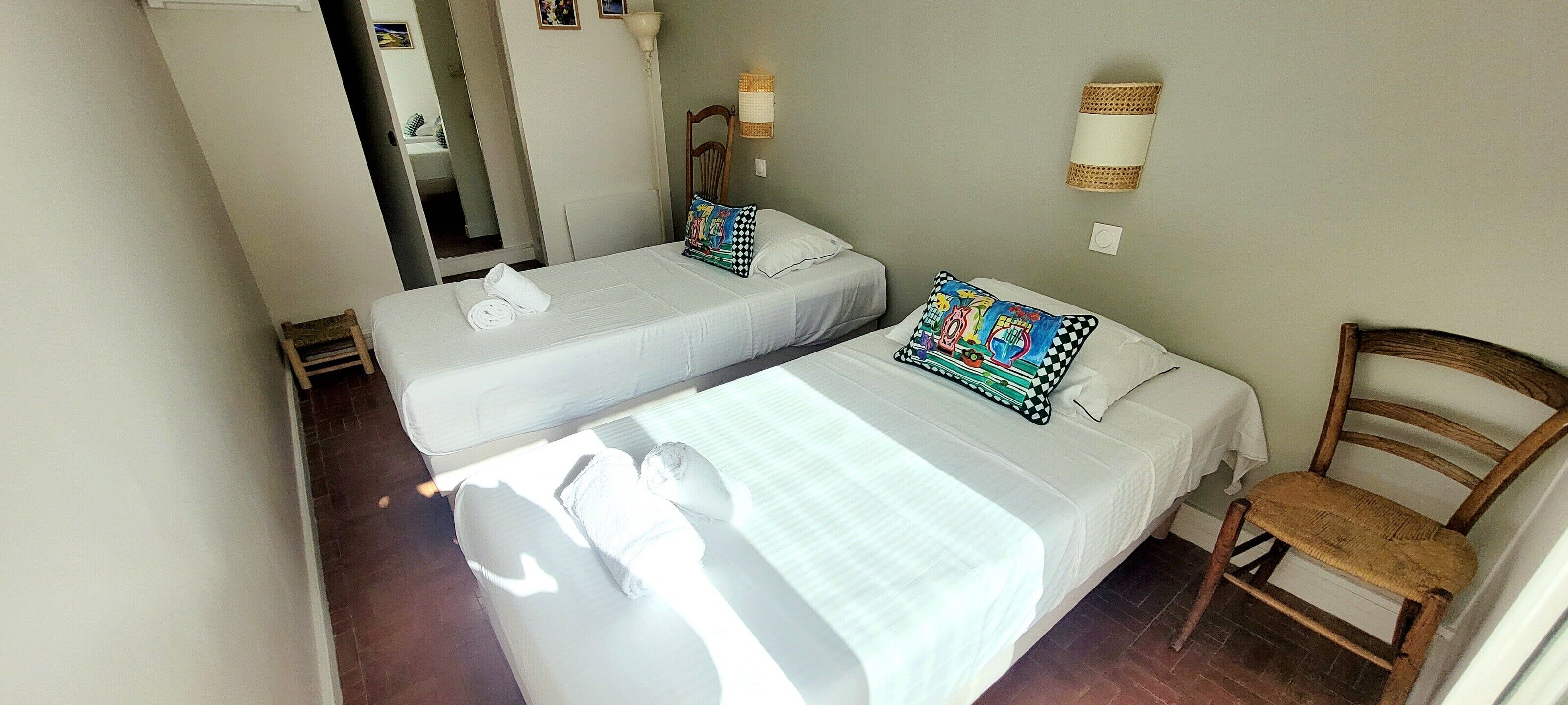 Ein Hotelzimmer mit zwei Einzelbetten, einem Holzbett, einem kleinen Tisch und einer Wandlampe.