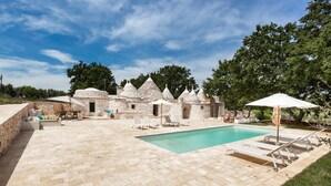 Uma área de piscina com edifícios de pedra, espreguiçadeiras e guarda-sóis.