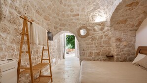 Quarto com paredes de pedra, uma cama, uma escada de madeira e vista através de um arco.