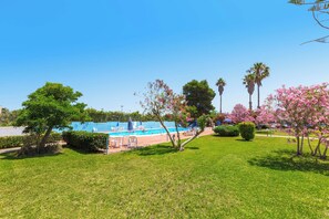 A pool area with a clear blue sky, surrounded by green grass and trees with pink flowers.