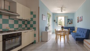 Una cocina funcional con estufa, horno y armarios blancos. Hay un comedor con mesa, sillas y un sofá azul.