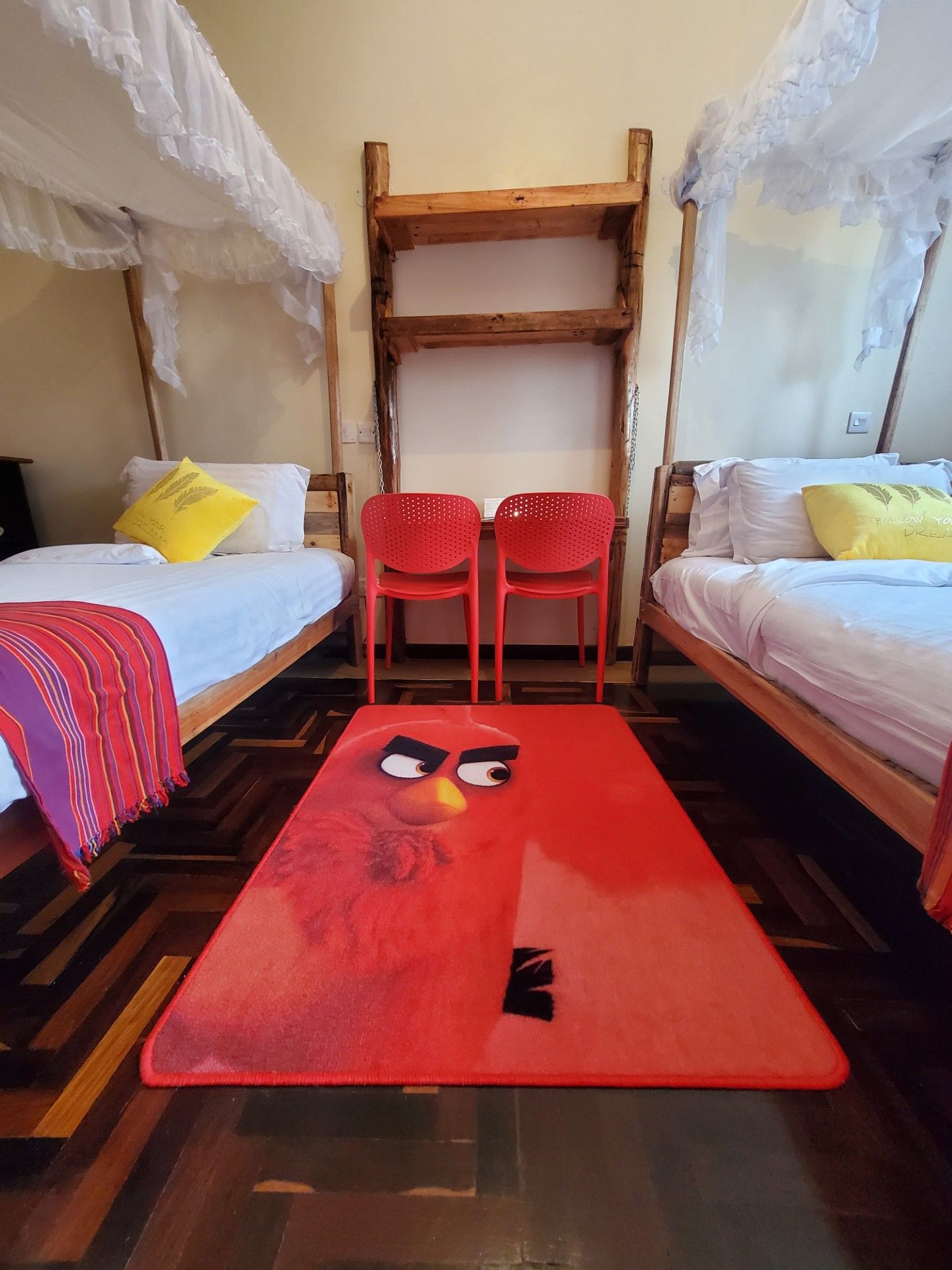 Een kamer met twee bedden, een houten bankje en een rood tapijt met een tekenfilmfiguur.