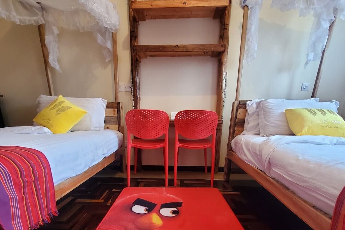 Una habitación con dos camas, cada una con ropa de cama blanca y un almohadón amarillo. Hay una alfombra roja con un personaje de caricatura en el centro.