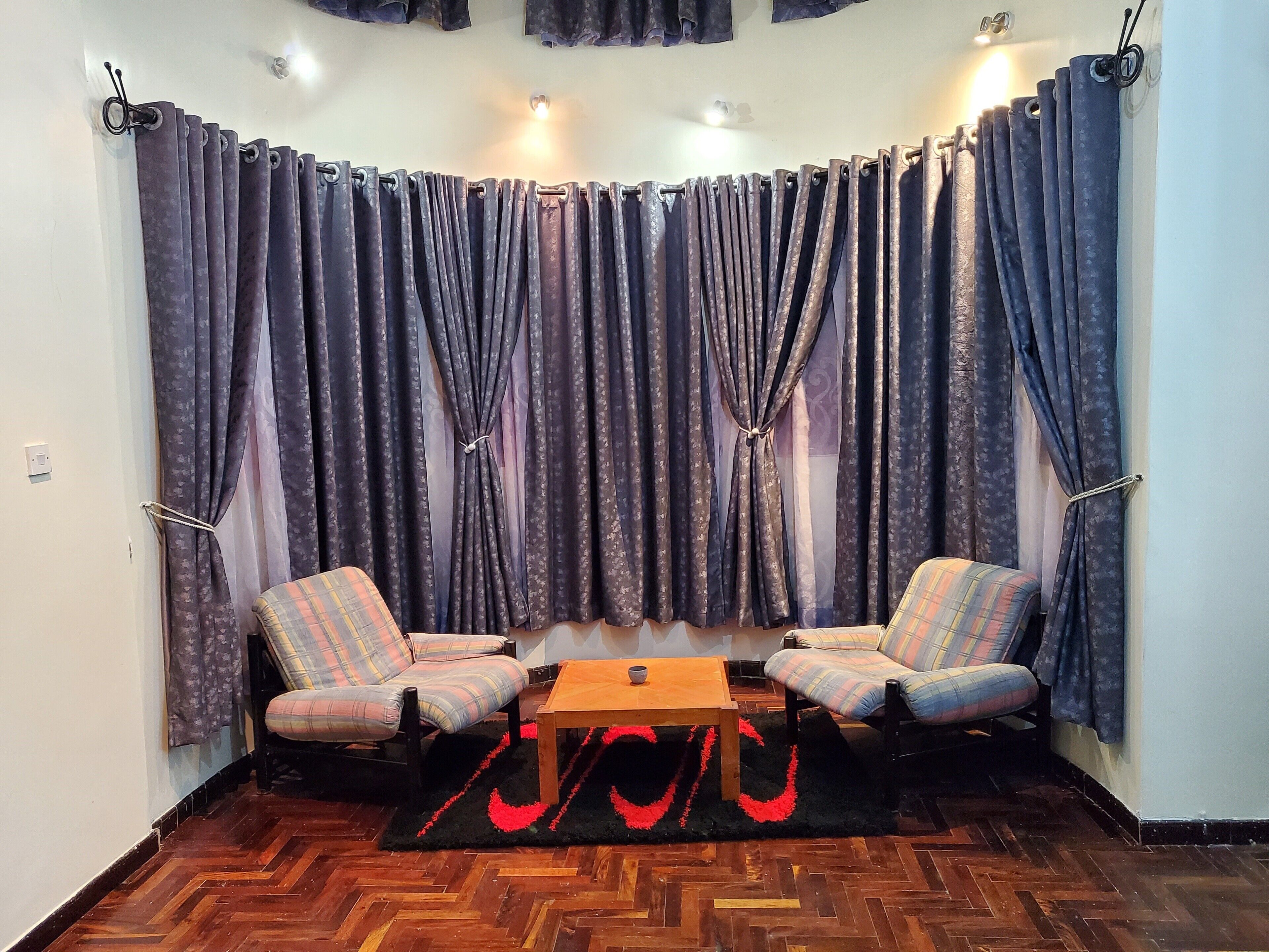 A corner room with two plaid chairs, a wooden table, and a black rug with red heart designs.