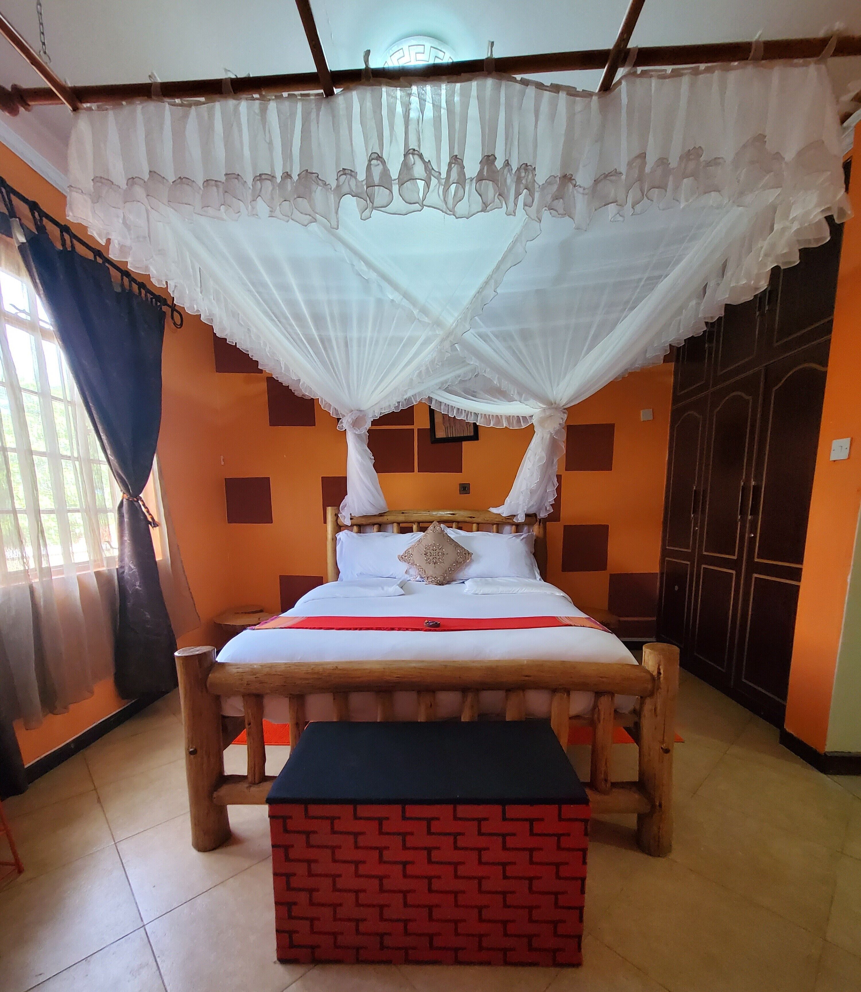 A bed with a canopy, a bench, and a wall with a geometric pattern.