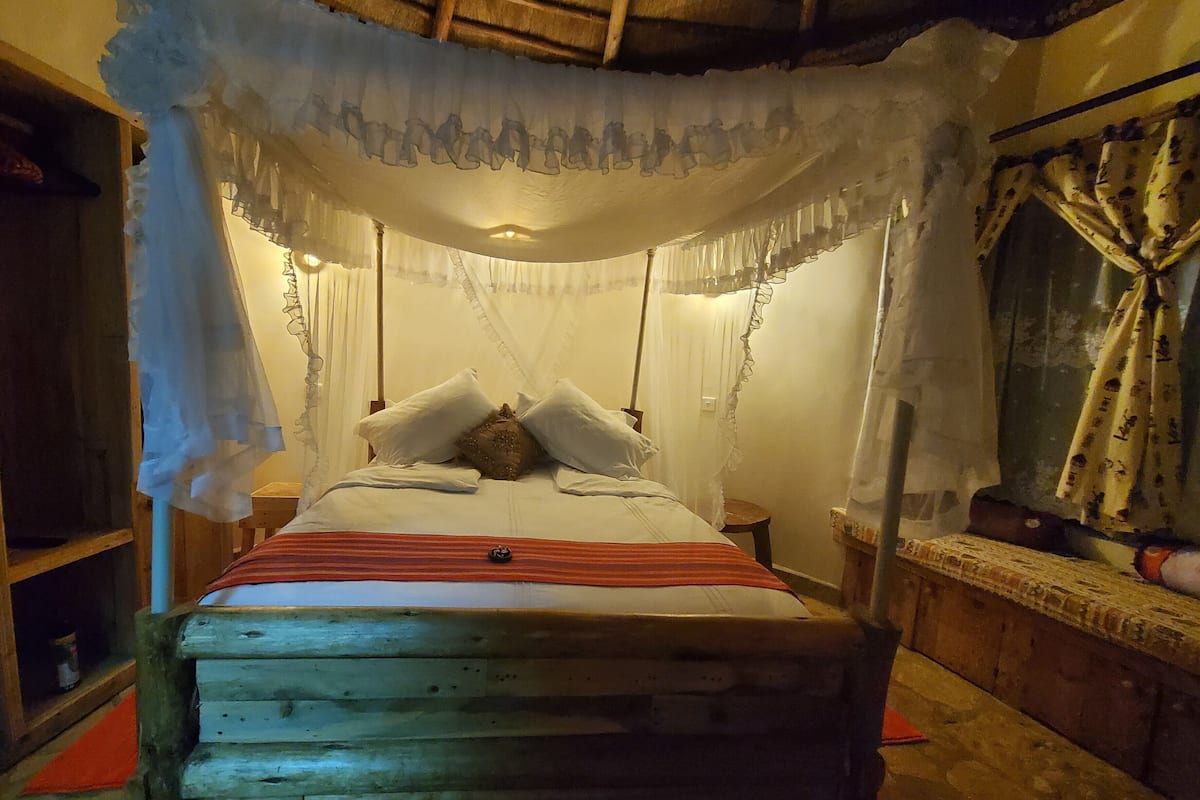 Una cama con dosel, cabecera de madera y mesita de noche con lámpara.