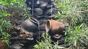 A rustic outdoor water feature with multiple clay pots and a small pond surrounded by greenery. - Edaala Comfort (Nairobi)