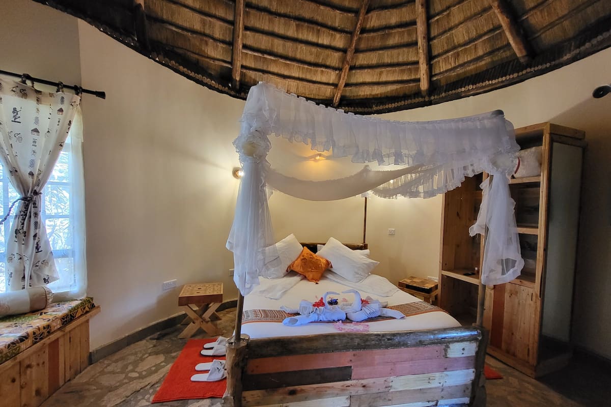 Una habitación con una cama bajo un dosel, un armario de madera, una mesita y una ventana con cortinas.
