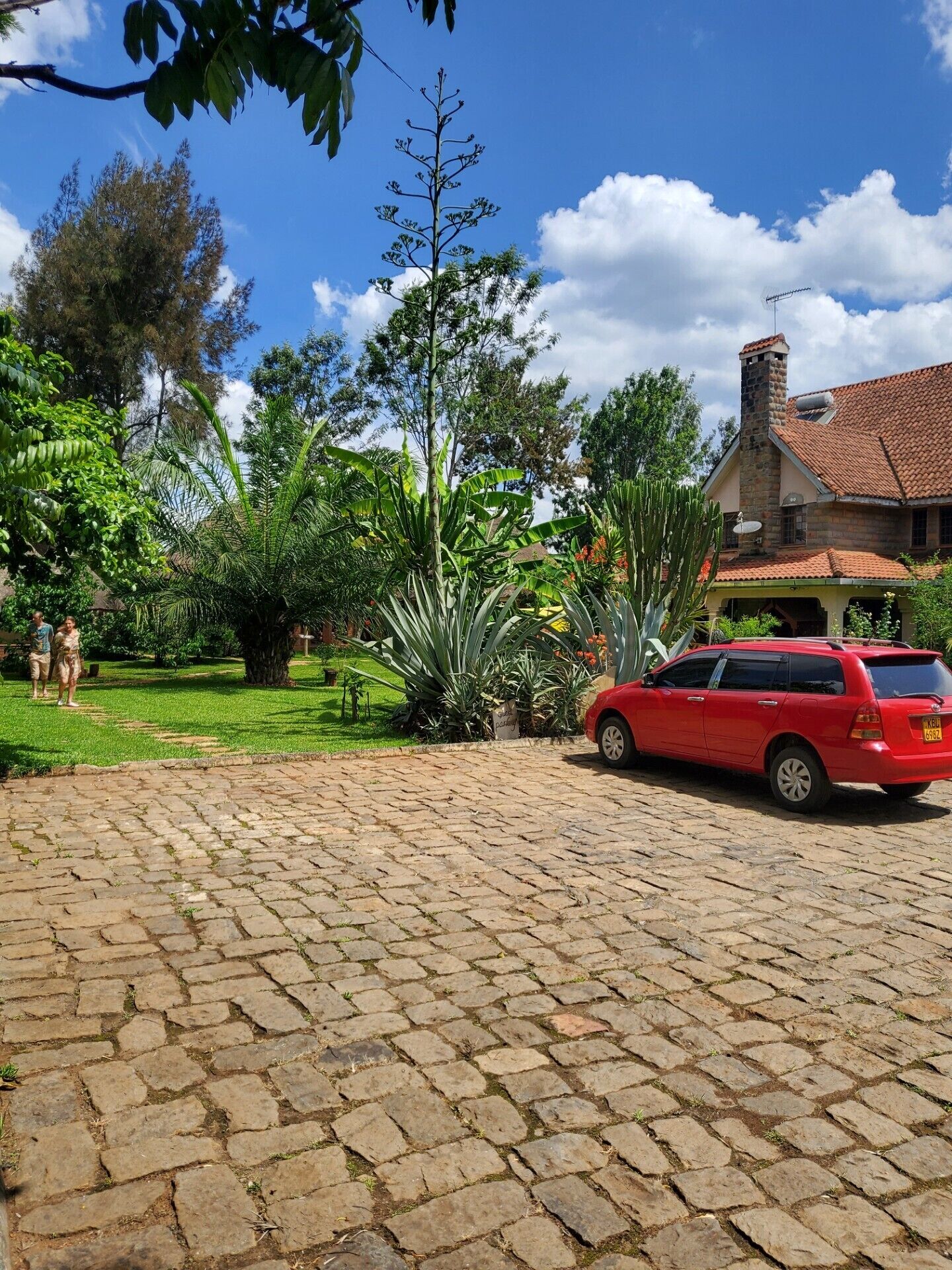A red car parked in front of a house with a stone chimney and a tiled roof.