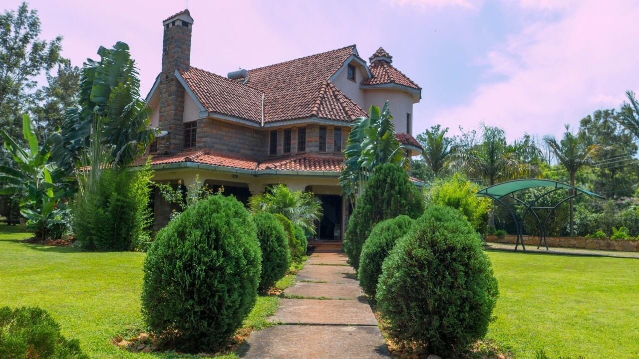 A large, two-story house with a stone facade and a tiled roof, surrounded by well-maintained gardens and a clear pathway leading to the entrance.