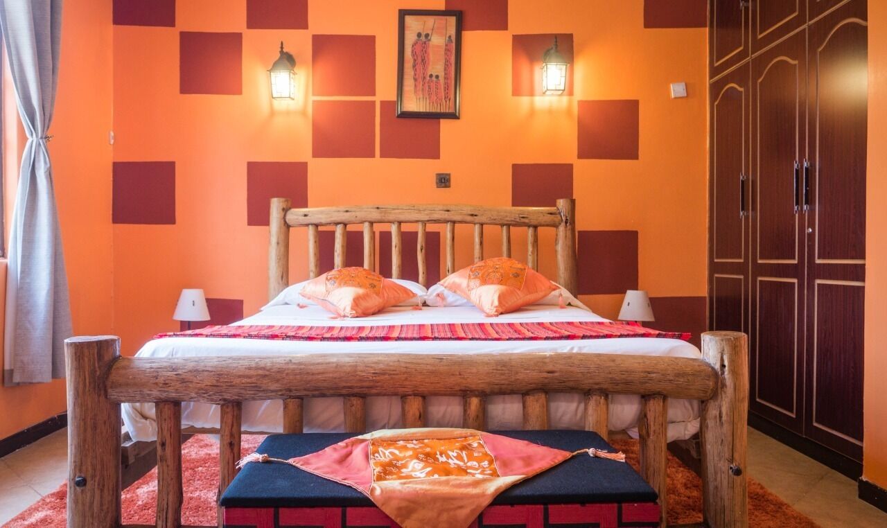 Ein Zimmer mit einem hölzernen Bett, zwei Nachttischlampen, einem rot-schwarz gemusterten Teppich und einem Schrank mit Spiegel.